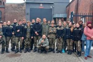 Na zdjęciu widoczni są uczestnicy zajęć oraz funkcjonariusz Służby Więziennej na dziedzińcu więziennym.

